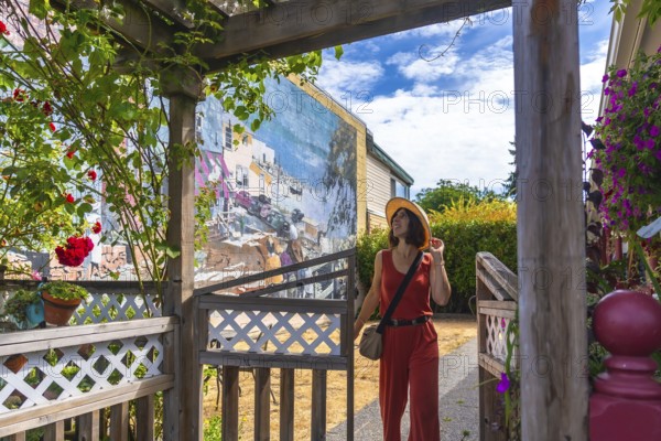 Female tourist wearing jumpsuit and straw hat walking through wooden gate and admiring colorful