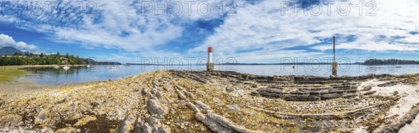 Rocky coastline stretches towards a red and white lighthouse, with sailboats dotting the tranquil