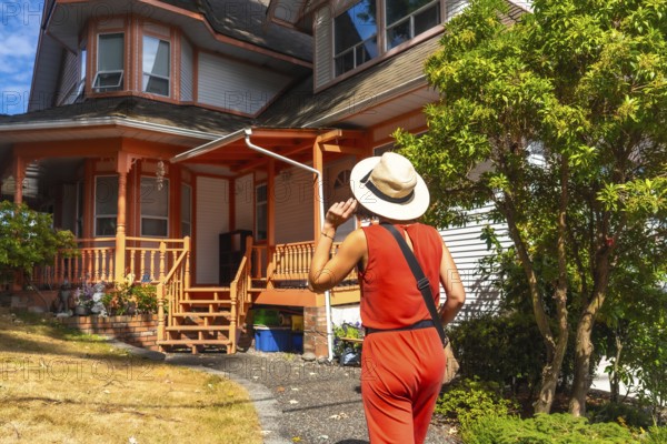 Female tourist wearing a straw hat and a red jumpsuit walking near a colorful wooden house in