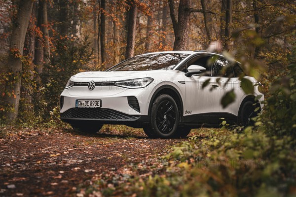 White car parked in forest surrounded by autumn leaves, VW ID4 electric car, Deer Carsharing, Calw,