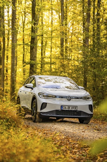 An SUV drives on a forest path in autumn surrounded by yellow leaves under bright sunlight, VW ID4