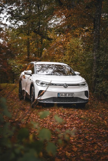 A white Volkswagen on a forest path covered with leaves in autumn, VW ID4 electric car, Deer