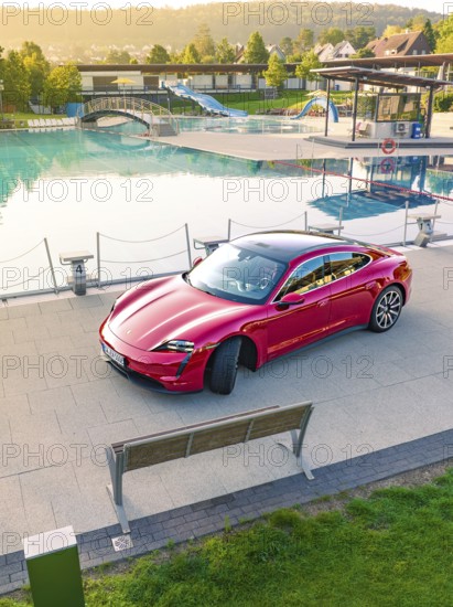 Red sports car parked next to a swimming pool and park bench in daylight, Porsche Taycan, Deer