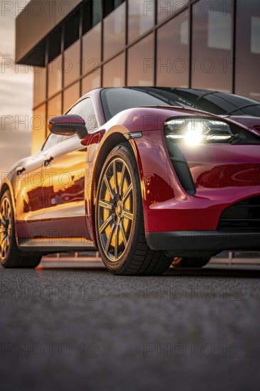 Red sports car reflected in front of a glass façade at sunset, Porsche Taycan, Deer Carsharing,