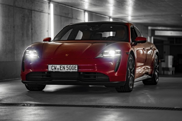 Red Porsche Taycan in underground car park at night with bright headlights and urban look, Porsche