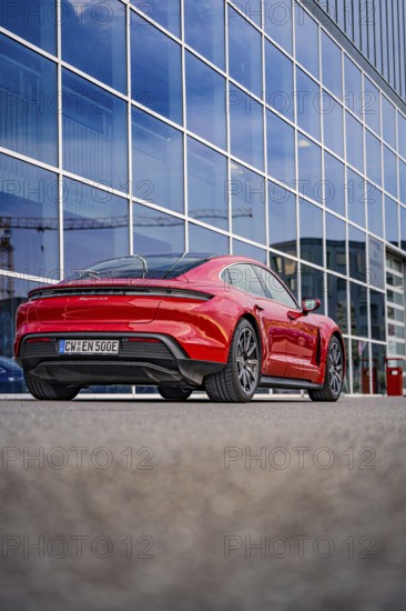Modern red car in front of a building with glass façade, urban atmosphere, Porsche Taycan, Deer
