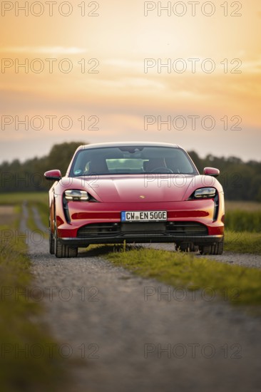 Front view of a red sports car on a gravel path at sunset, Porsche Taycan, deer car sharing. Calw,