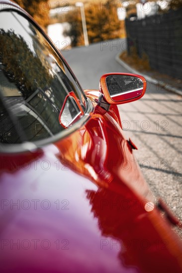 Red car with side mirror on a road with reflections, Porsche Taycan, Deer car sharing. Calw,