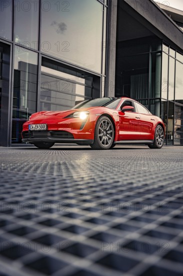 Red sports car in front of a modern glass building at dusk, Porsche Taycan, deer car sharing. Calw,