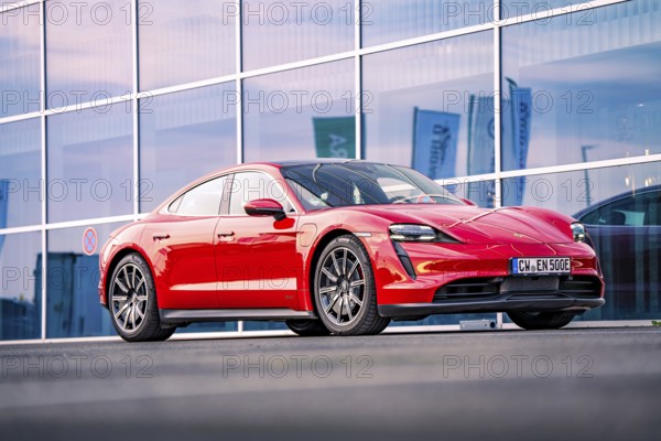 Red sports car in front of a modern glass façade at dusk, Porsche Taycan, deer car sharing. Calw,