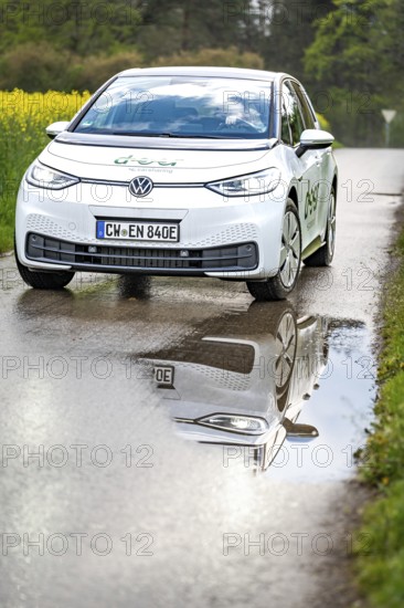 Car on wet road with clear reflection in the puddle, surrounded by green nature, ID3 VW, deer car