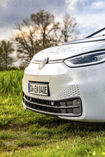 Close-up of a car nose with raindrops on green field in front of trees, ID3 VW, deer car sharing.