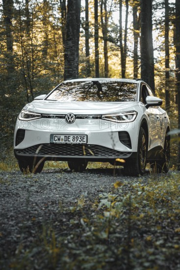 A white car is parked on a gravel path in the forest at dusk, VW ID4 electric car, Deer Carsharing,