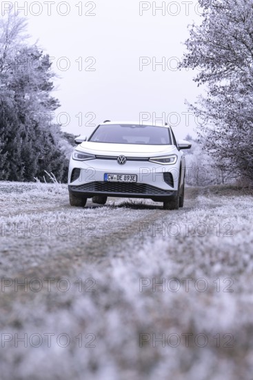 White car in a field with hoarfrost and bare trees in the background, VW ID4 electric car, Deer