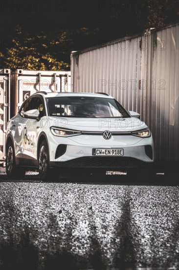 A car on a gravel field next to stacked containers in the shade, VW ID4 electric car, Deer