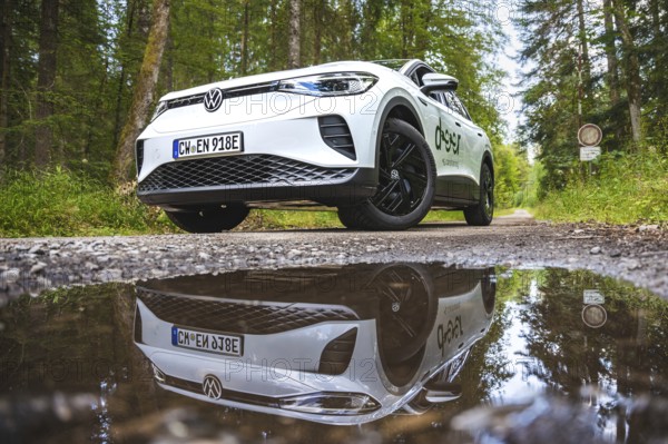 White car in the forest reflected in a puddle on the ground, VW ID4 electric car, Deer Carsharing,