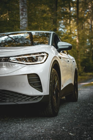 White car in the forest, front view with clear tire display, VW ID4 electric car, Deer Carsharing,