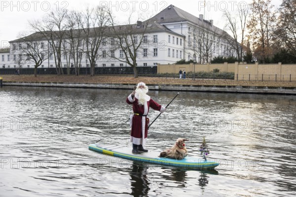 A water sports enthusiast dressed up as Santa Claus rides a SUP on the Spree in front of Bellevue