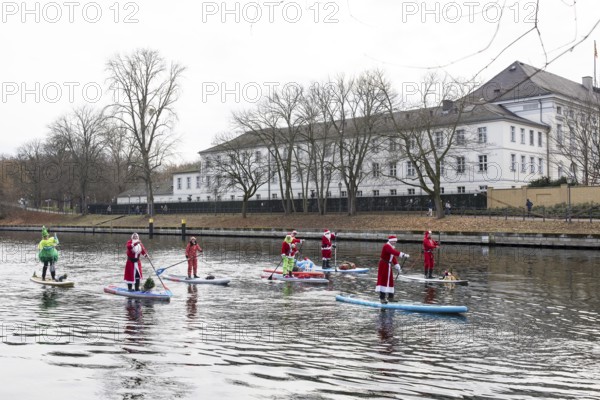 Water sports enthusiasts dressed up as Santa Claus ride SUPs on the Spree in front of Bellevue
