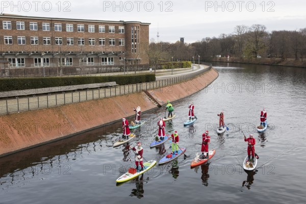 Water sports enthusiasts dressed up as Santa Claus ride SUPs on the Spree am Park at the