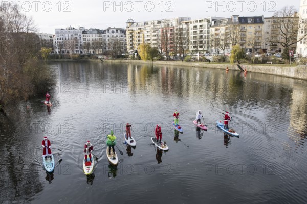 Water sports enthusiasts dressed up as Santa Claus ride SUPs on the Spree on the banks of the