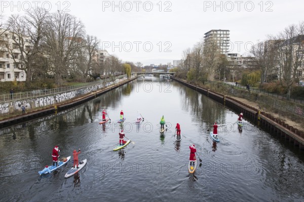 Water sports enthusiasts dressed up as Santa Claus ride SUPs on the Spree on the banks of the Hansa