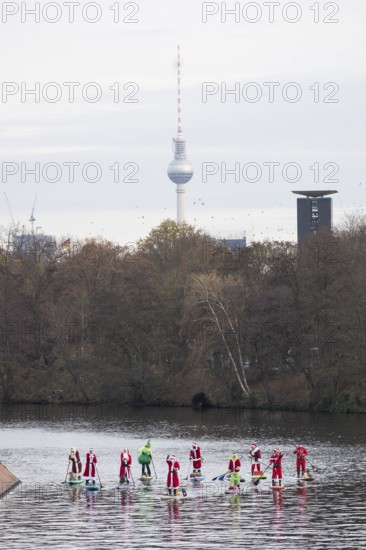 Water sports enthusiasts dressed up as Santa Claus ride SUPs on the Spree am Park at the