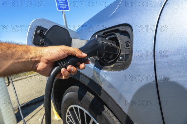 Hand inserting power cable into electric vehicle at a vehicle charging station, promoting