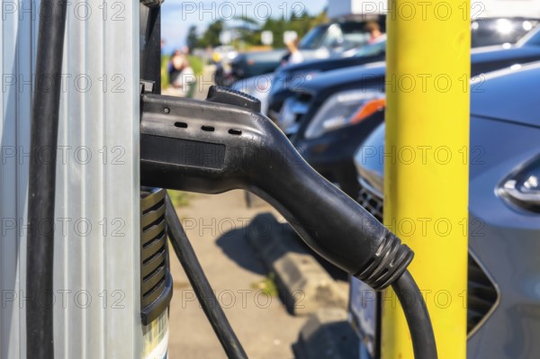 Electric vehicle charger hanging on a charging station, waiting to be plugged into a car, with cars