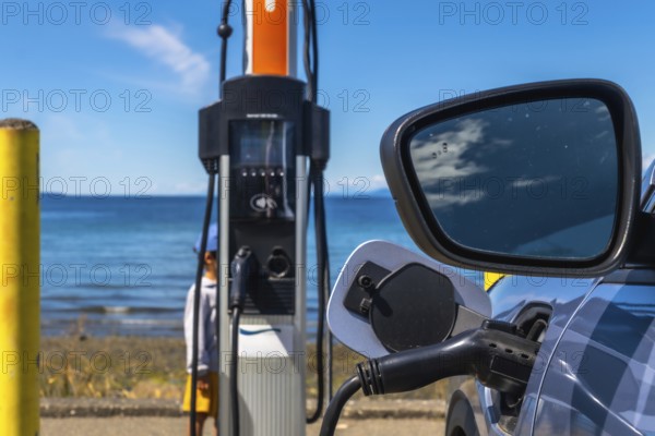 Modern electric vehicle connected to a charging station on the coast with a beautiful ocean view,