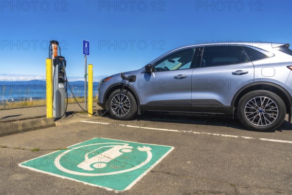 Silver electric car charging at a station by the sea, showcasing a picturesque ocean view while