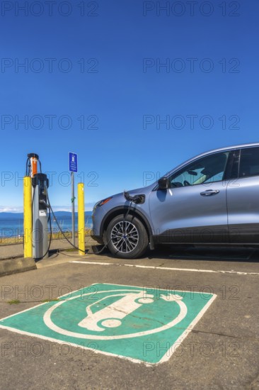 Modern electric car charging at a seaside station on a bright sunny day, highlighting the