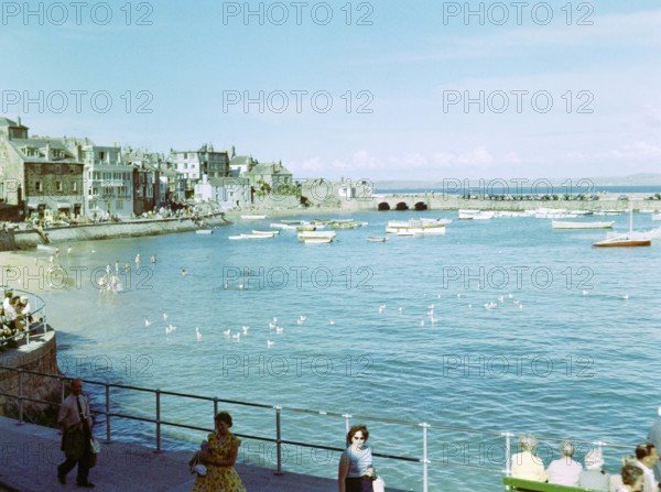 Boats at moorings in the harbour people swimming in sea from beach at St Ives, Cornwall, England,
