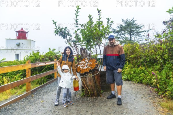 Happy family posing near the wild pacific trail sign with amphitrite point lighthouse in the