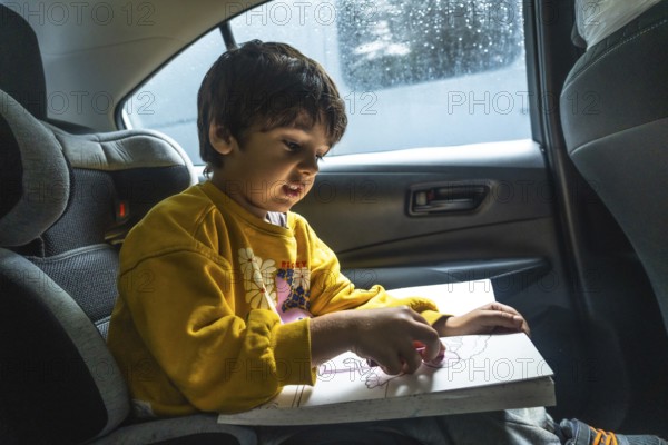 Young child concentrating on creating colorful artwork with crayons while secured in a car seat,