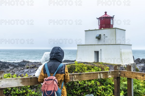 Two tourists in raincoats and backpacks enjoying the misty view of amphitrite point lighthouse,