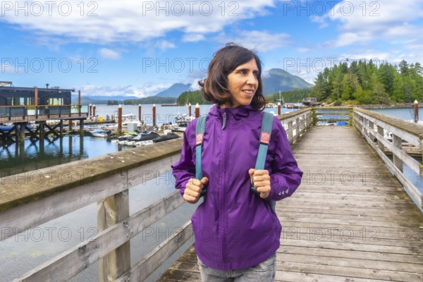 Female tourist wearing a purple jacket and carrying a backpack walking along a wooden pier in
