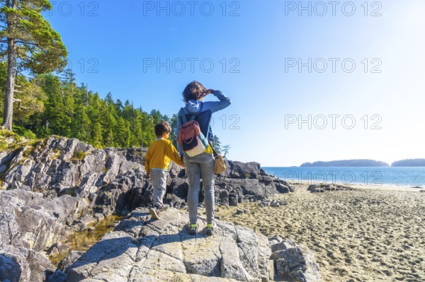 Mother and son holding hands. Exploring the beautiful rocky coastline near a sandy beach in tofino.