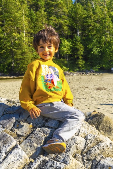 Happy child enjoying summer vacation, sitting on a rock at the beach in tofino, vancouver island,