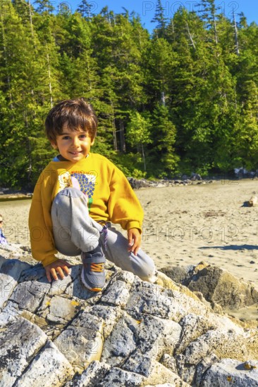 Young boy sitting on a large rock at a beach in tofino, british columbia, soaking up the summer sun