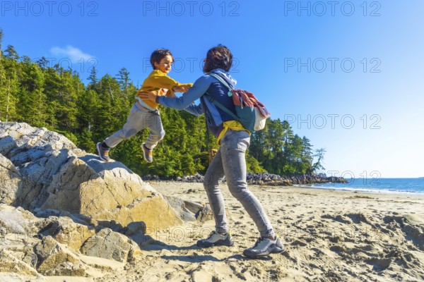 Mother catching her son as he joyfully jumps from a rock on a sandy beach, surrounded by lush green