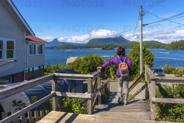 Female tourist with backpack walking down wooden stairs enjoying scenic view of tofino inlet,