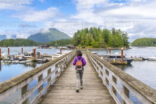 Female tourist with backpack walking down a wooden pier in tofino, british columbia, with boats,