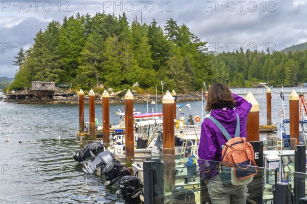 Tourist in a purple jacket and backpack capturing photos of the scenic tofino harbor, featuring