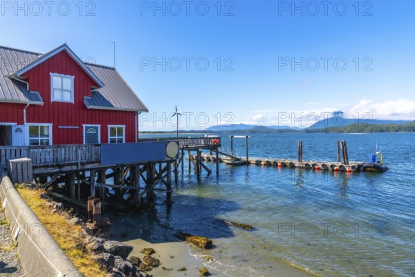 Calm, clear blue water lapping against the shore complements a vibrant red wooden building and pier