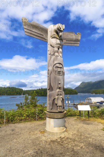 Wooden totem pole featuring intricate carvings of a thunderbird and other figures, rising against a
