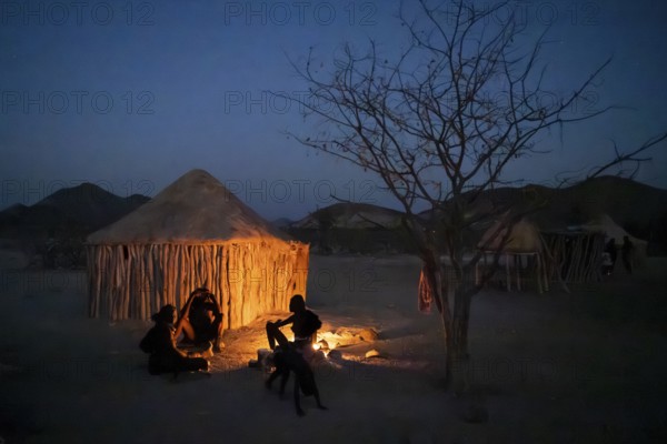 Himba at the campfire in the evening, night view, Himba huts, traditional Himba village in the
