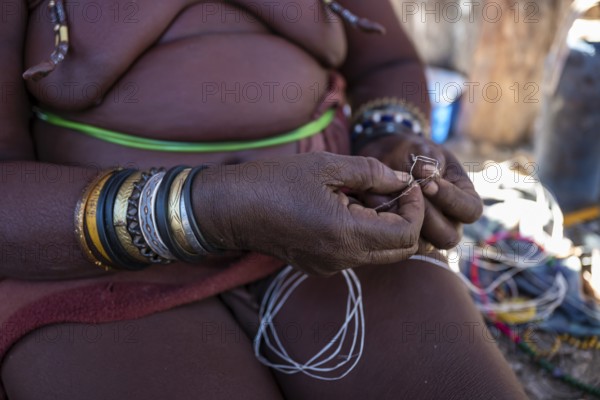 Himba woman doing handiwork, making hand bands for tourists, traditional Himba village, Kaokoveld,
