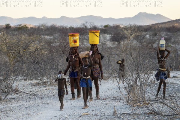 Himba woman and children run to fetch water with canisters through dry countryside, traditional