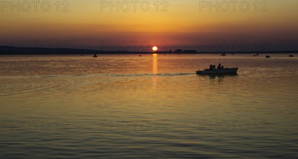 Boat over calm waters at sunset, orange dusk, Steinhude Steinhuder Meer